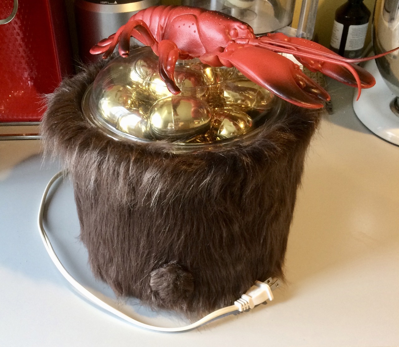 a fur-covered crock pot full of golden eggs with a lid with a lobster for a handle